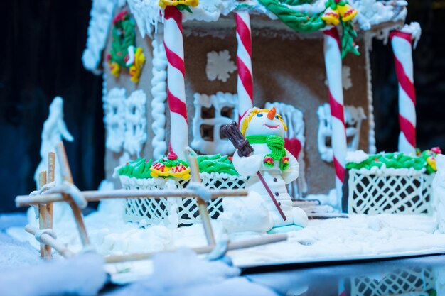 밤에 진저브레드 하우스 근처의 설탕 매스틱에서 눈사람을 닫습니다. 계절 제안 및 휴일 엽서 모형