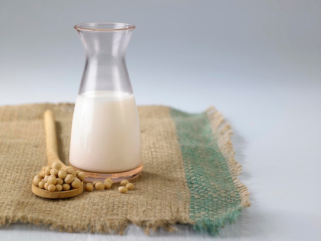 Photo close-up of soy milk with soybeans on burlap against white background