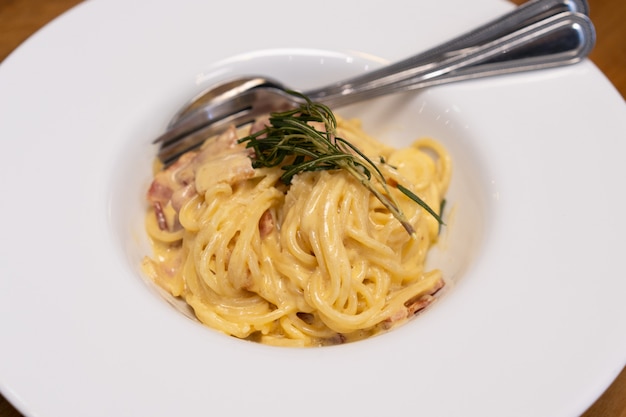 Foto chiuda in su della salsa di cabonara degli spaghetti in zolla bianca sulla tabella di legno.