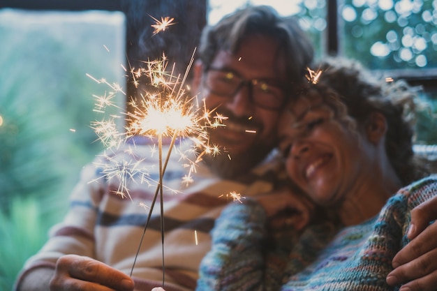 Close up of sparkler light and couple smiling in background at home