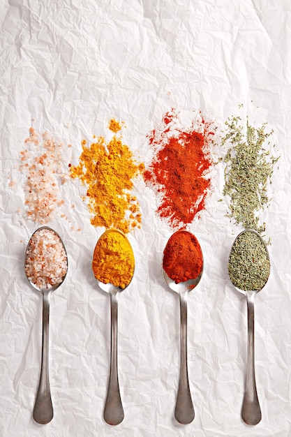 Photo close-up of spices in spoons arranged on white paper