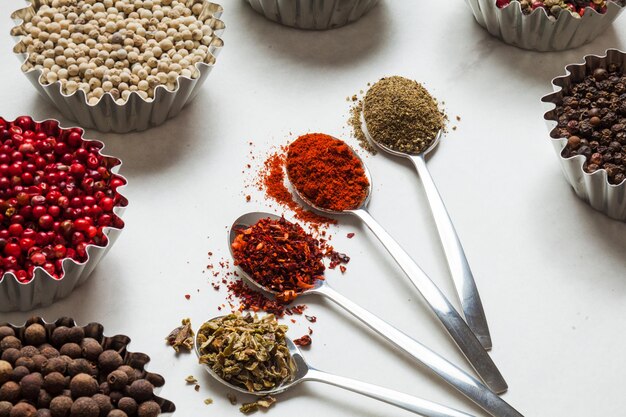 Close up of spices in spoons on white marble table. Different types of pepper