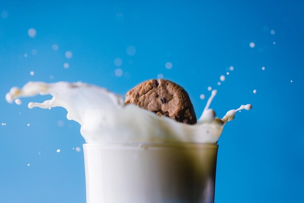 Photo close-up of spilled milk with cookie in glass against blue background, copy space