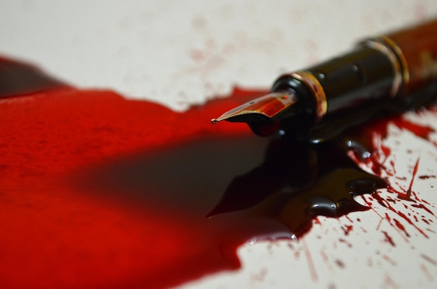 Foto close-up di inchiostro rosso e penna spruzzati sul tavolo