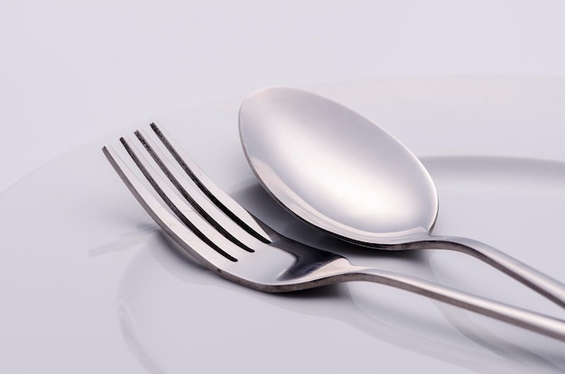 close-up of spoon and fork in plate against white background