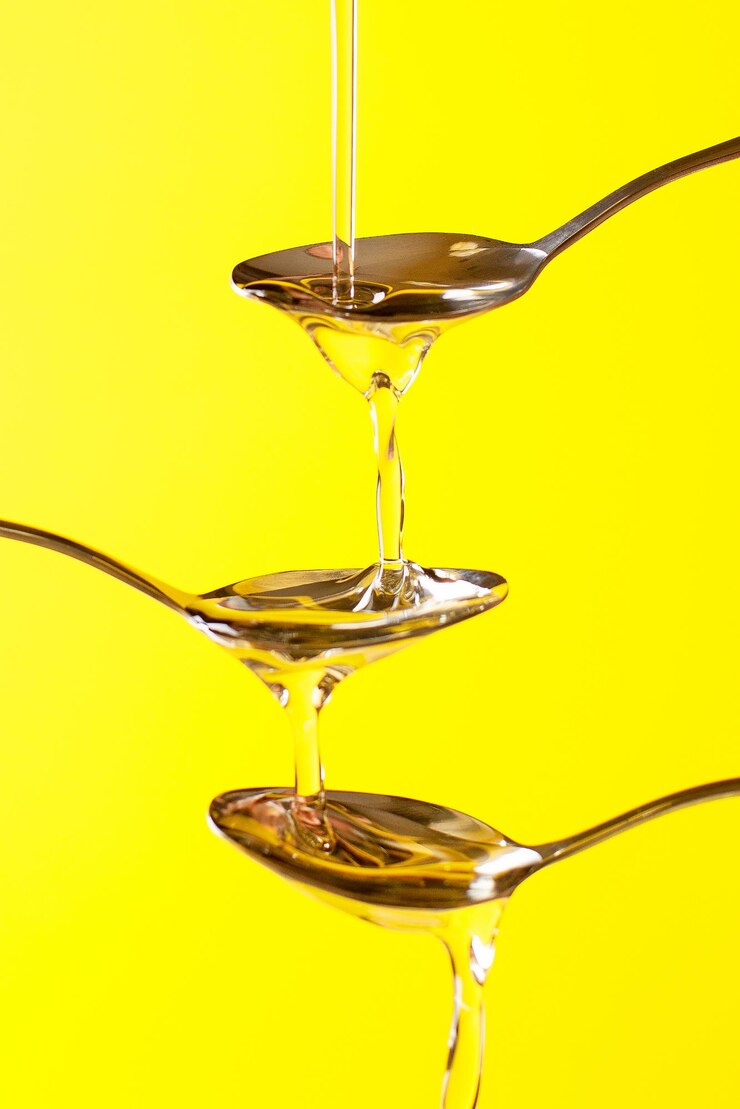 Close up on spoons on which liquid honey is poured on a yellow background