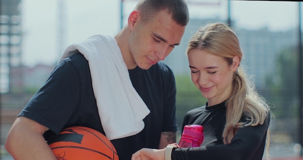 Close up of sports man and fit woman friends on basketball court after training checking results on smartwatch and looking at the camera Concept of sport power competition active lifestyle