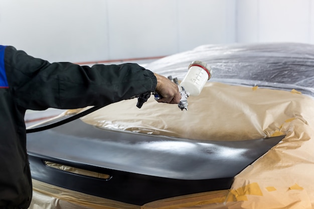 Close-up of a spray gun with black paint for painting a car in a special booth