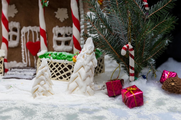 Close up of a sprig of Christmas tree and a sugar mastic trees near gingerbread house on dark background. Mockup for seasonal offers and holiday post card