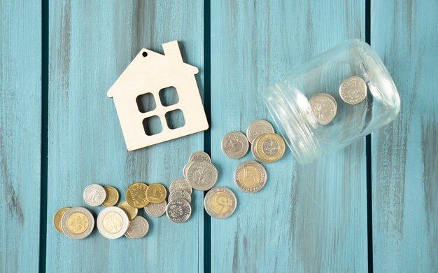 Close-up of stacked coins and house figurines on wooden surface, savings concept.