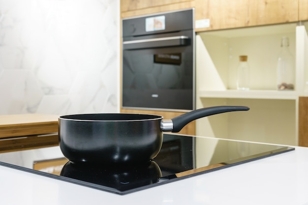 Photo close-up of stainless steel cooking pot and pan on induction hob in modern kitchen.