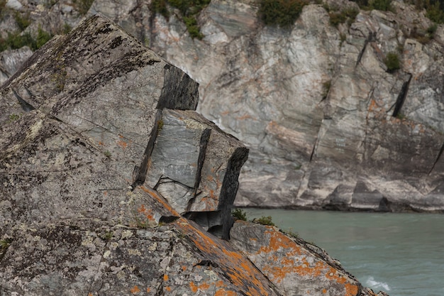 Close-up of a steep sharp rock with greenery against the backdrop of a fast mountain river.