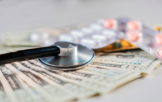 Close up of stethoscope with pills on dollar bills High cost of medical health with stethoscope Stethoscope with medicines on dollar bills