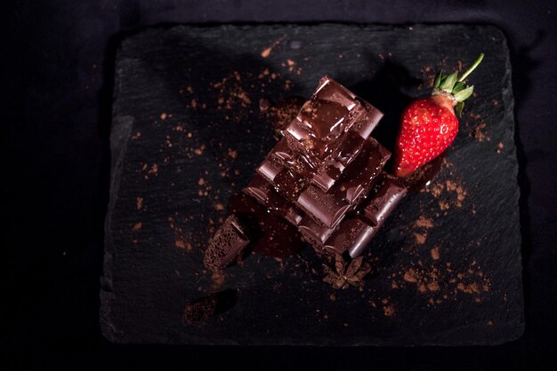 Close-up of strawberries with chocolate on table against black background