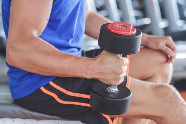 Close up strong arm holding and lifting dumbbell at the gym