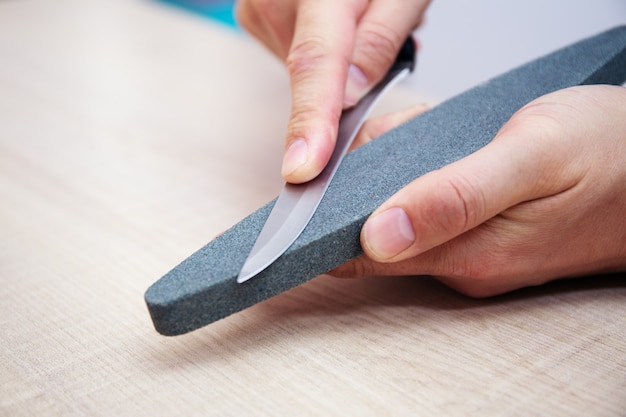 Photo close-up strong male hands sharpen a kitchen metal knife with a grindstone. home household knife sharpening.