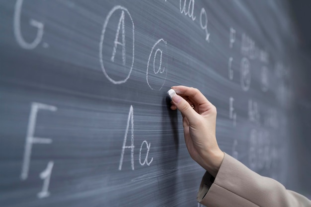 a close up students hand holding piece of chalk and writing on blackboard