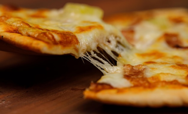 Close-up studio opname met houten lepel schil oppakken van hete oven gebakken smakelijke heerlijke Italiaanse zelfgemaakte ham en ananas Hawaiiaans zacht brood korst pizza stuk van houten plaat pan op restaurant tafel