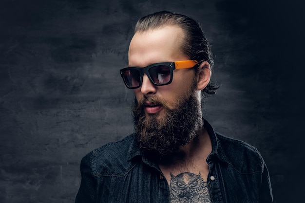 Close up studio portrait of bearded hipster male in sunglasses over dark grey background.