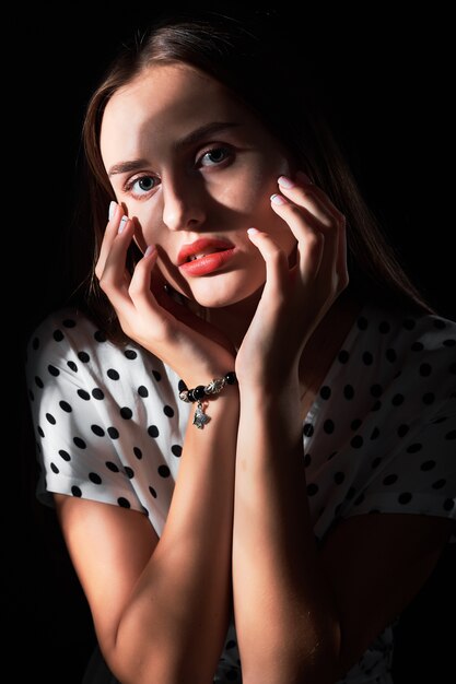 Close-up studio portrait of a young girl with long hair and red lips against black.