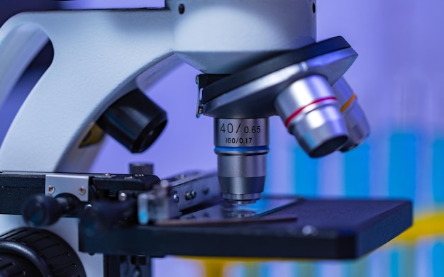 Close-up studio shot van vergrootglas zoomlens Microscoop camera plaatsen op werktafel in ziekenhuis laboratorium vol glaswerk apparatuur reageerbuis rek Erlenmeyer bekerglas en computermonitor.