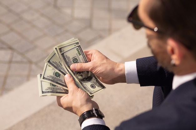 Крупным планом успешного американского бизнесмена, рассматривающего пачку 100-долларовых банкнот, сидя