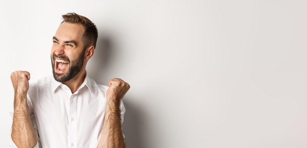 Foto close-up di un uomo caucasico di successo che si rallegra facendo pompa di pugno e urlando di gioia guardando a sinistra vincente in piedi sopra la persona bianca sullo sfondo