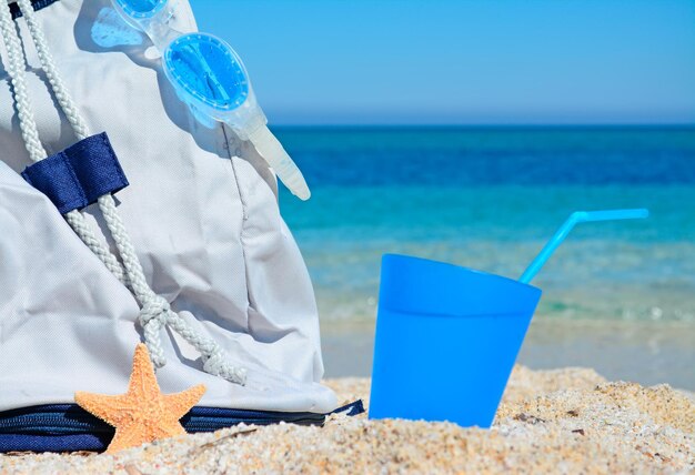 Photo close up of a summer bag with drink and goggles