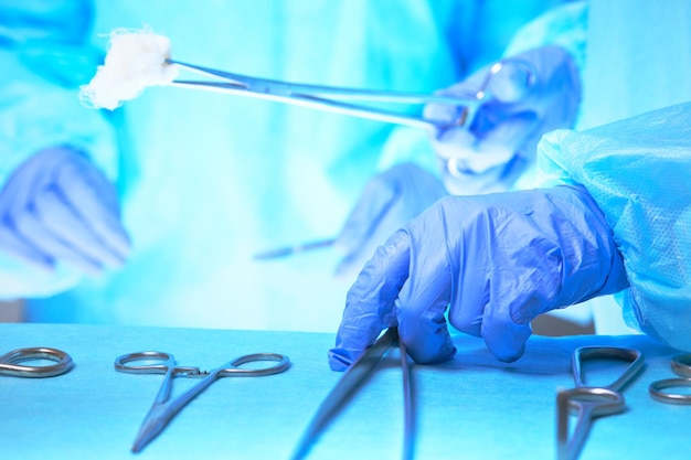 파란색 톤의 수술실에서 일하는 외과 의사의 손을 클로즈업. 수술을 수행하는 의료 팀