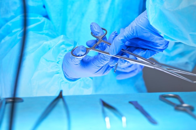 青を基調とした手術室で働く外科医の手のクローズアップ。手術を行う医療チーム