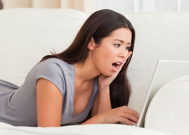 close up of a surprised woman lying on sofa with notebook in front of her