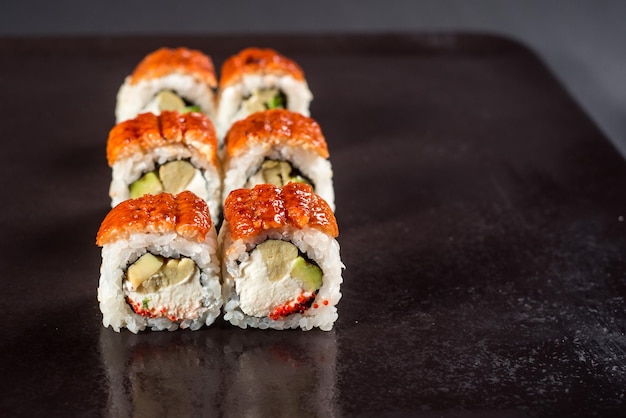 Close up sushi rolls in a black plate on dark background