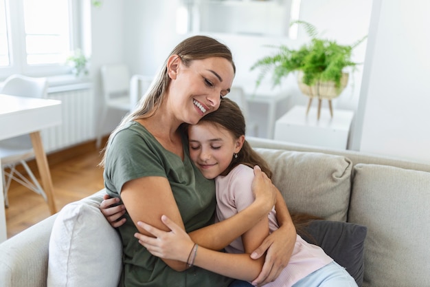 Close up of sweet pretty daughter cuddling with her young mother. Lovely mother embracing her cute daughter on the sofa at home.