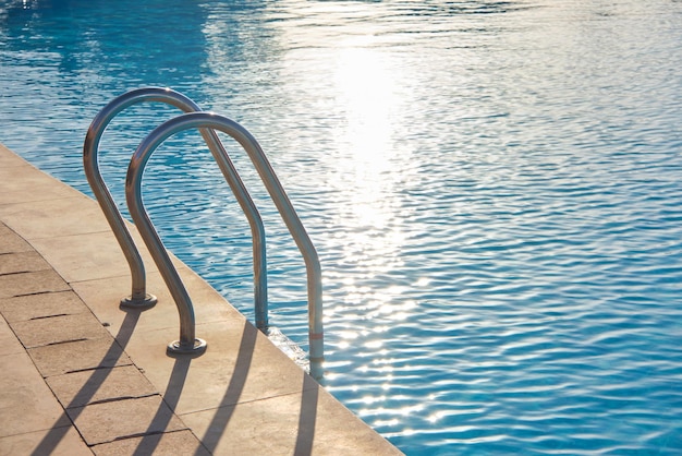 Primo piano del corrimano in acciaio inossidabile della piscina che scende nell'acqua chiara della piscina tartaruga. accessibilità del concetto di attività ricreative.