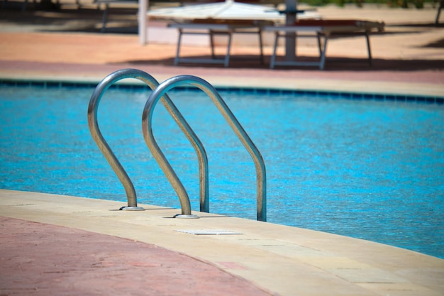 Close up of swimming pool stainless steel handrail descending into tortoise clear pool water. Accessibility of recreational activities concept.