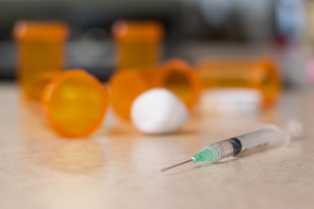 Close up of syringe with empty bottles of drugs in the background