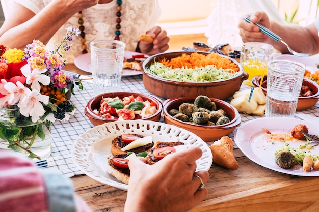 Primo piano di un tavolo pieno di cibo vegetariano fresco con un gruppo di persone che mangiano insieme