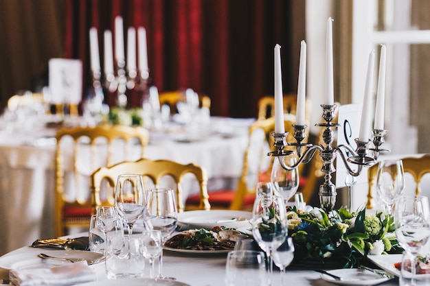 Close up of table served for festive dinner decorated with candlestick plates glasses and flowers Banquet table with dish in luxurious restaurant Table setting for people on special occasion