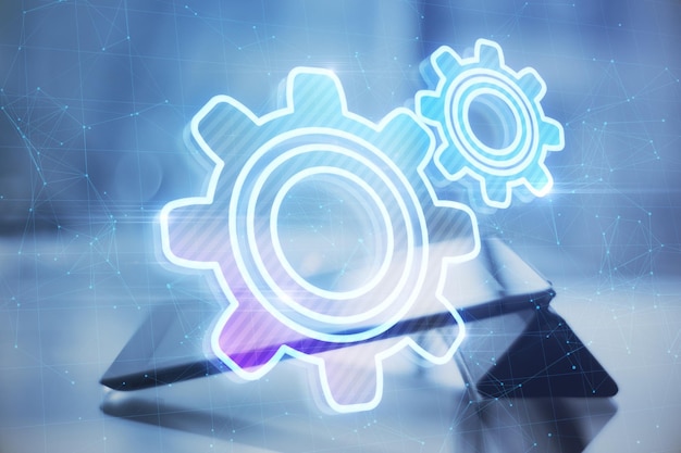 Close up of tablet at desktop with abstract glowing gear wheels on blurry background with connections Digital engineering and industry concept Double exposure