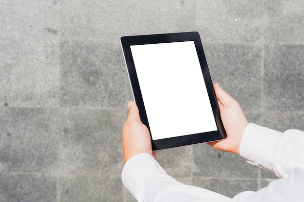 close-up tablet mockup with a white screen in the hands of a businessman against the background of a concrete wall.