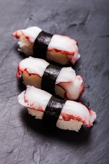 Close-up of Tako nigiri sushi with cooked octopus on a black slate background