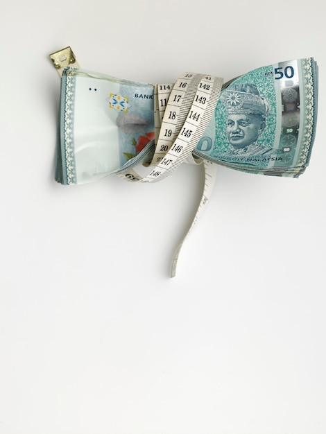 Close-up of tape measure rolled up on paper currency over white background