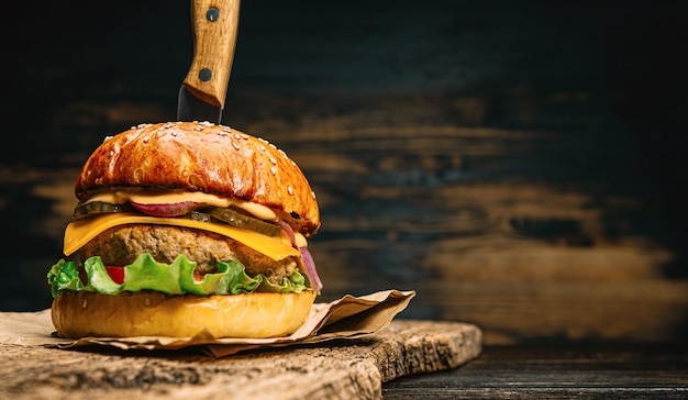 Close up tasty beef burger on a wooden table with a knife inserted into it