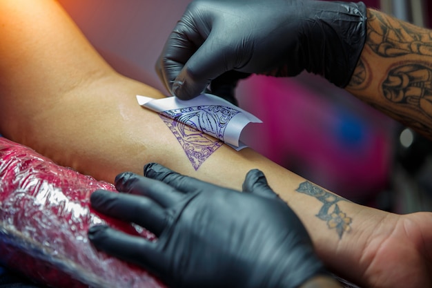 Close up tattoo artist demonstrates the process of getting black tattoo with paint. Master works in black sterile gloves.