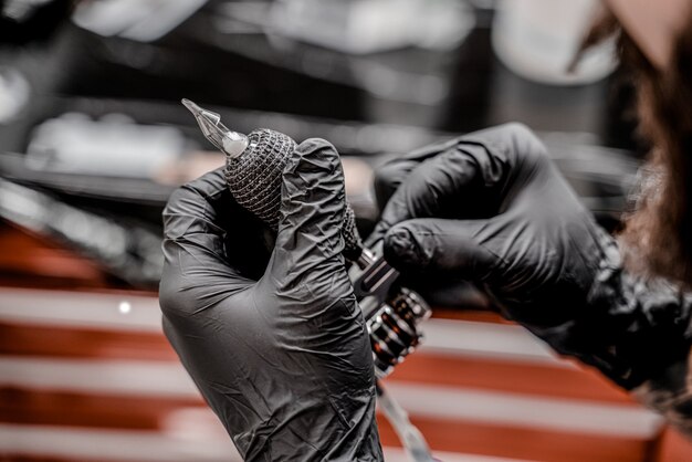 Close up tattooer in black gloves preparing tattoo machine for work in modern tattoo studio.