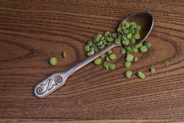 Photo close up teaspoon with green split peas grains on wood. raw uncooked fresh cereals.