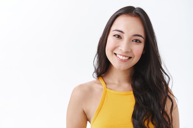 Close-up tedere, vrouwelijke Oost-Aziatische brunette met lang haar, schuin hoofd en glimlachend met aangename, vriendelijke blik, luisterende klant of zakelijke bijeenkomst en beantwoorden van vragen met plezier