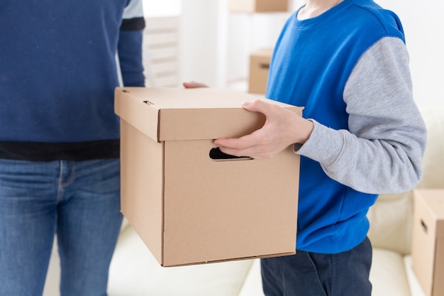 Close-up of teen boy holds a box and a pot of plants while moving to a new apartment. Housewarming