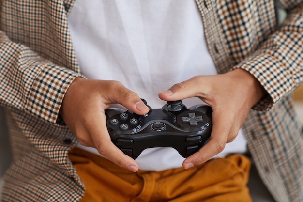 Foto primo piano di un adolescente afro-americano che tiene in mano il gamepad mentre gioca ai videogiochi a casa, copia spazio