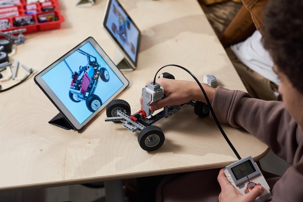 Primo piano di un ragazzo adolescente che costruisce robot in classe di ingegneria presso una scuola moderna e utilizza la tavoletta digitale per la programmazione, lo spazio di copia